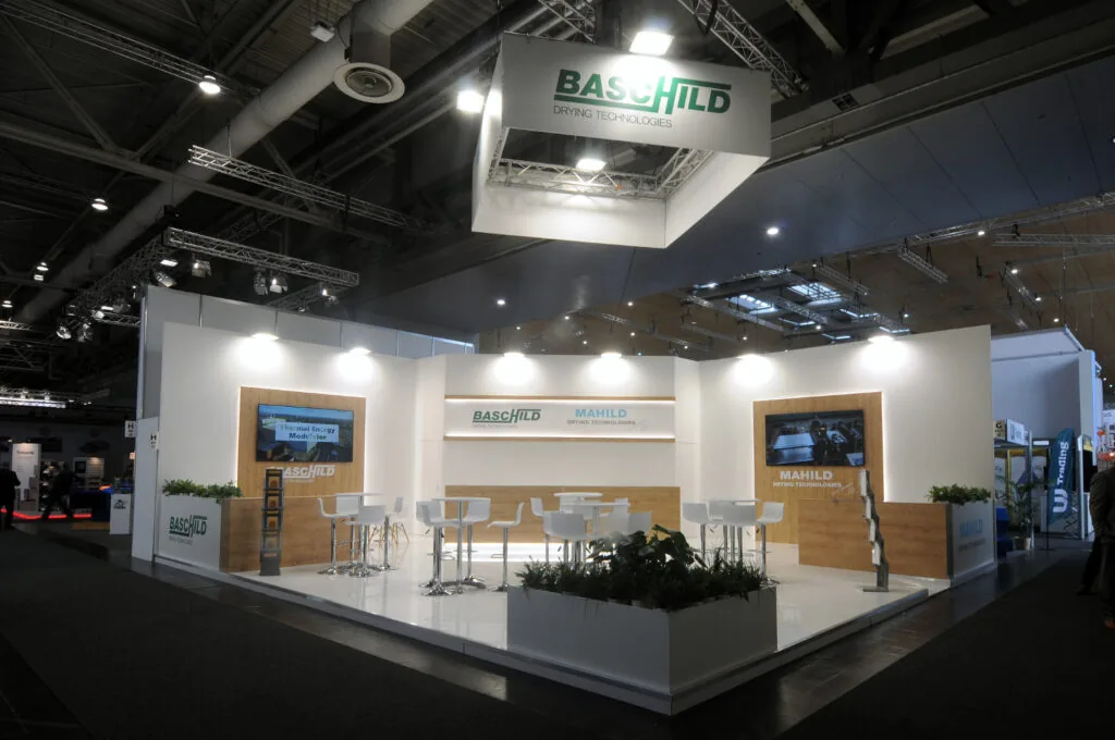 Stand fieristico moderno BASCHILD e MAHILD con design bianco, schermi digitali e piante decorative, esposto in una fiera tecnologica.