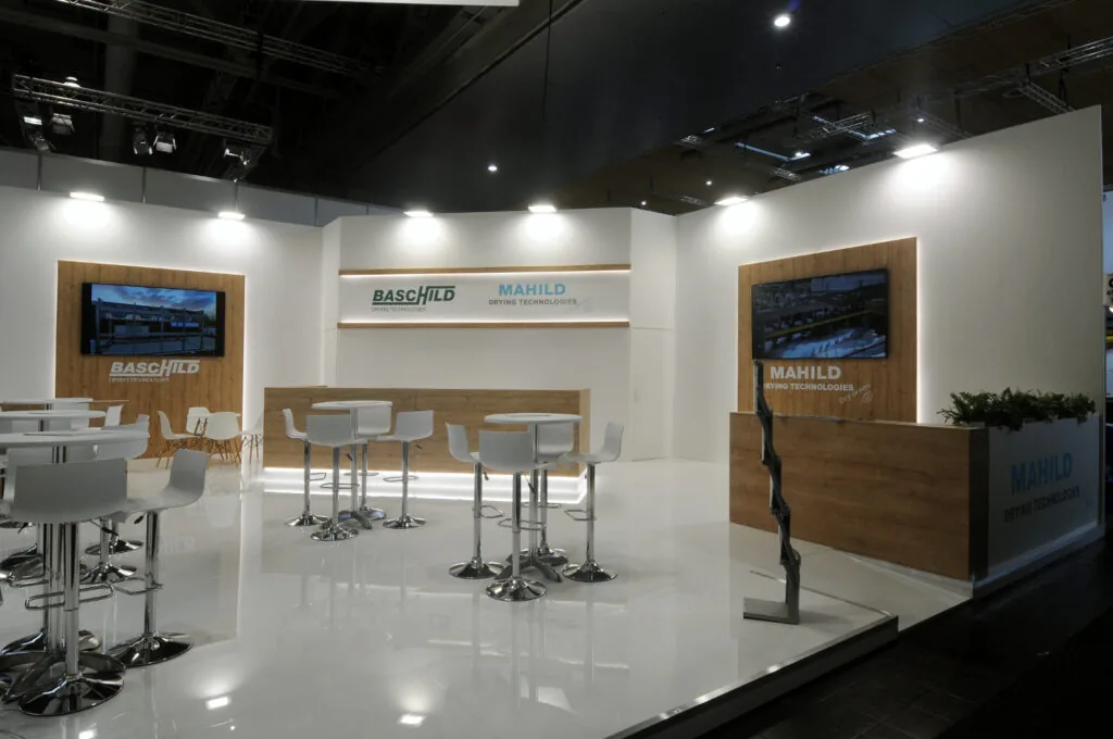 fiera ligna - stand bashild mahild Stand fieristico moderno con arredi in legno e bianco, illuminazione integrata e monitor digitali. Design professionale e accogliente, ideale per presentazioni aziendali e networking.