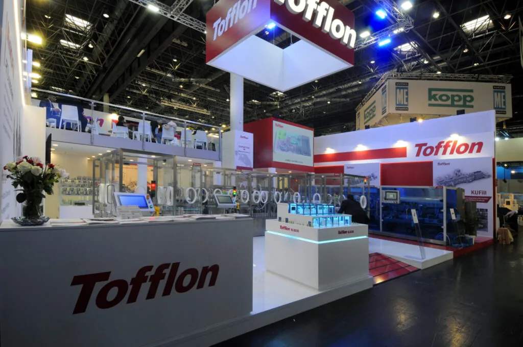 Stand espositivo Tofflon a Interpack con macchinari industriali, area accoglienza e branding aziendale per networking B2B.
