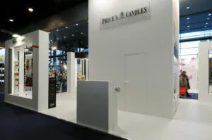 Ambiente 2026: chi sono le buyer personas Stand fieristico Price's Candles con candele profumate esposte su scaffali, design total white e illuminazione elegante