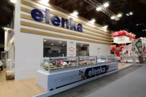 Stand espositivo Elenka a SIGEP: allestimento personalizzato con materiali moderni, illuminazione mirata e display digitale per promuovere prodotti artigianali da gelateria e pasticceria.