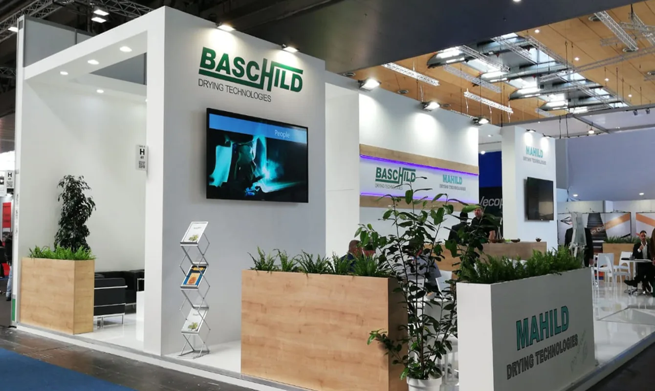 Stand BASCHILD e MAHILD alla fiera, con design moderno, schermo digitale, brochure e piante verdi.