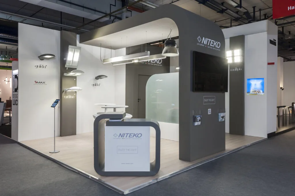 Stand fieristico NITEKO con illuminazione industriale, schermo digitale e desk promozionale, progettato per fiere ed eventi aziendali.