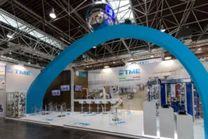Stand TME Packaging Solutions a Interpack: allestimenti fieristici per networking strategico e business B2B con arco blu e area espositiva moderna