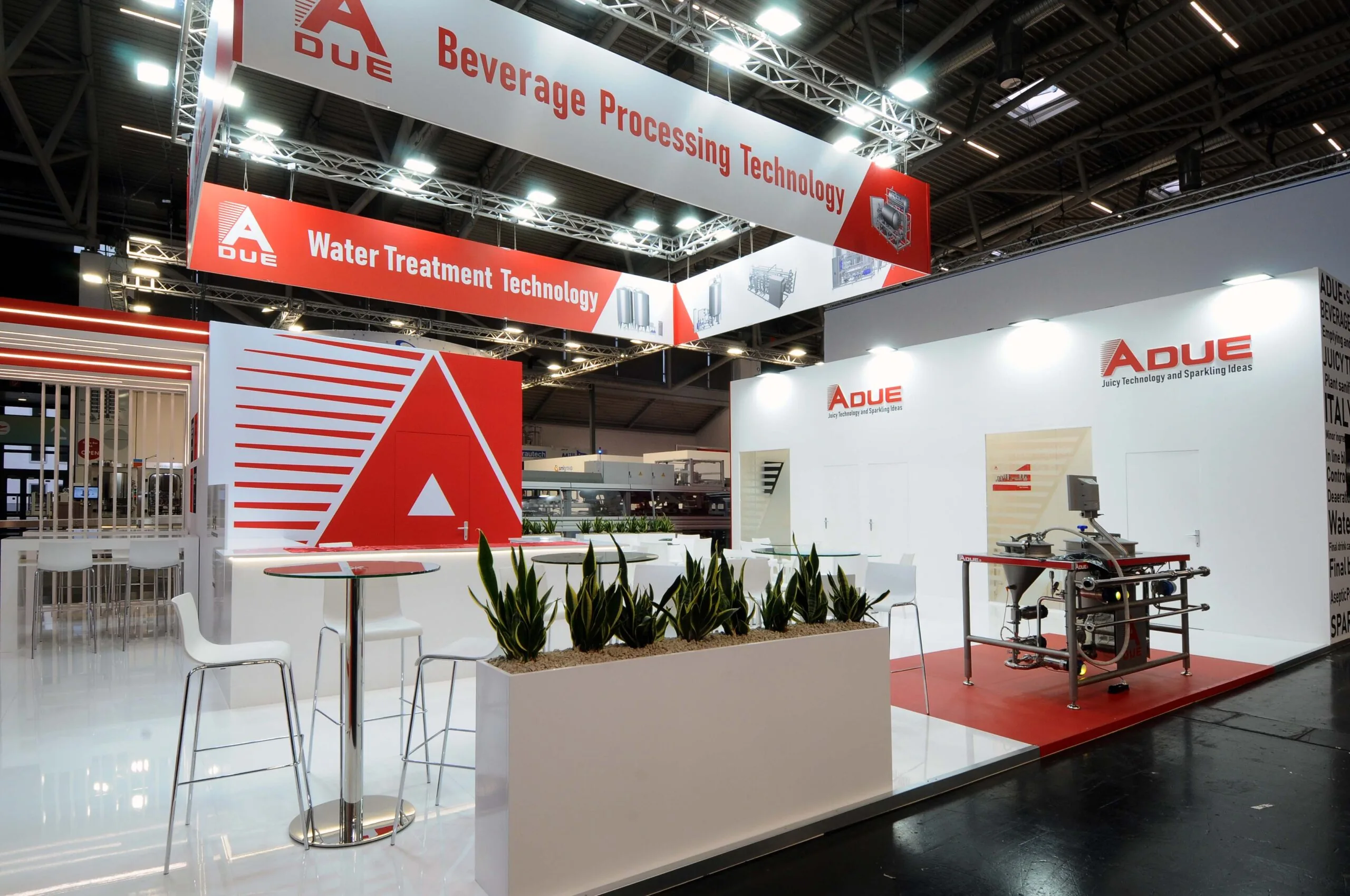 Stand ADUE con slogan “Drink Technology and Sparkling Ideas”, esposizione macchinari per il beverage e arredi bianchi in fiera industriale.